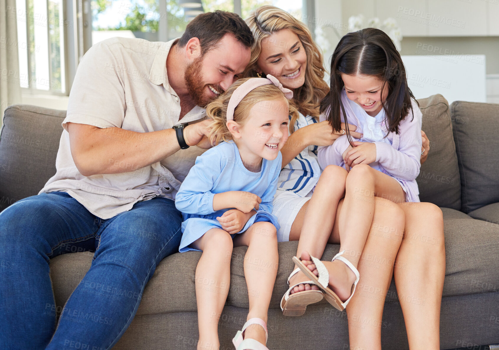 Buy stock photo Playful caucasian parents tickling their children while relaxing together on a sofa at home. Carefree little girls spending time with loving parents. Happy family having fun at home