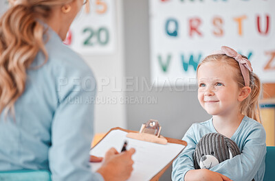 Young smiling caucasian child sitting with her psychologist in a clinic. Cute girl talking to a mental health professional. Using a clipboard to take notes on her patient. Dyslexia and anxiety