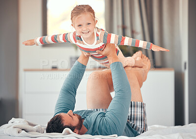 Playful little caucasian girl pretending to fly with arms outstretched while being lifted and carried by her dad at home. Man holding his excited daughter while having fun in pyjamas on bed at home