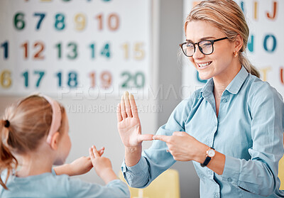 Buy stock photo Smiling caucasian teacher wearing spectacles communicating with deaf girl student with hand sign language in a classroom at school. Sign language teacher in a tutoring class for a cute female child with hearing disability
