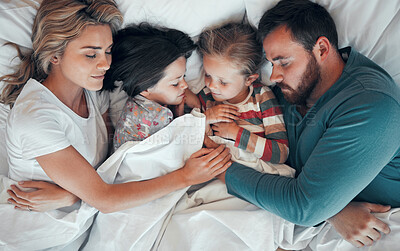 Sleeping caucasian family of four in pyjamas from above lying cosy together in bed at home. Loving parents cuddling two little kids for bedtime. Adorable girls taking a nap and rest with mom and dad
