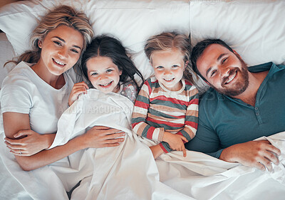 Buy stock photo Happy caucasian family of four in pyjamas from above lying cosy together in bed at home. Loving parents with their two little kids. Adorable young girls bonding with their mom and dad during bedtime