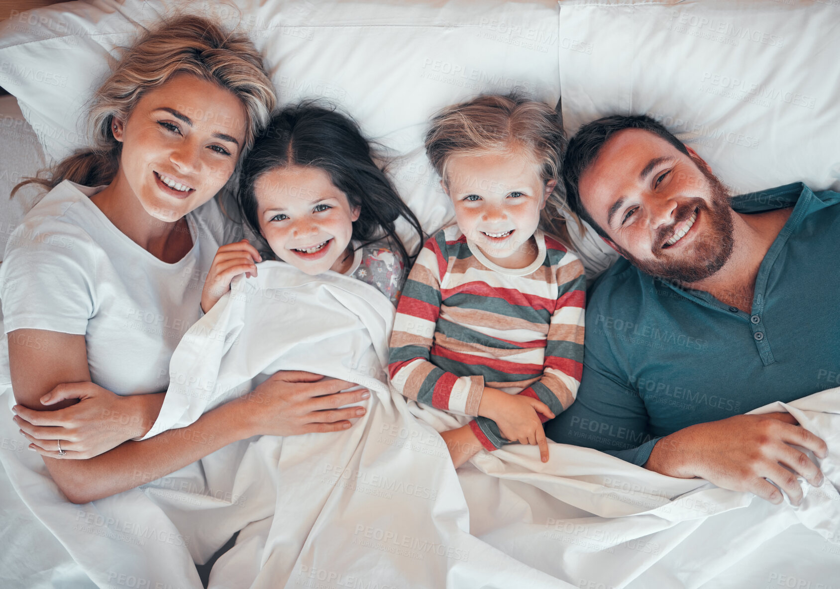 Buy stock photo Happy caucasian family of four in pyjamas from above lying cosy together in bed at home. Loving parents with their two little kids. Adorable young girls bonding with their mom and dad during bedtime