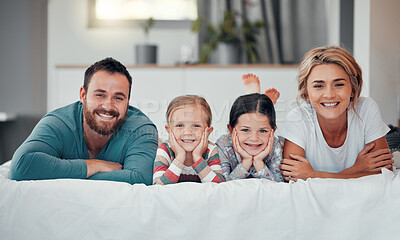 Portrait of a smiling young caucasian family lying close together on the bed at home. Happy adorable girls bonding with their mother and father on a weekend. Happy couple and daughters in the morning