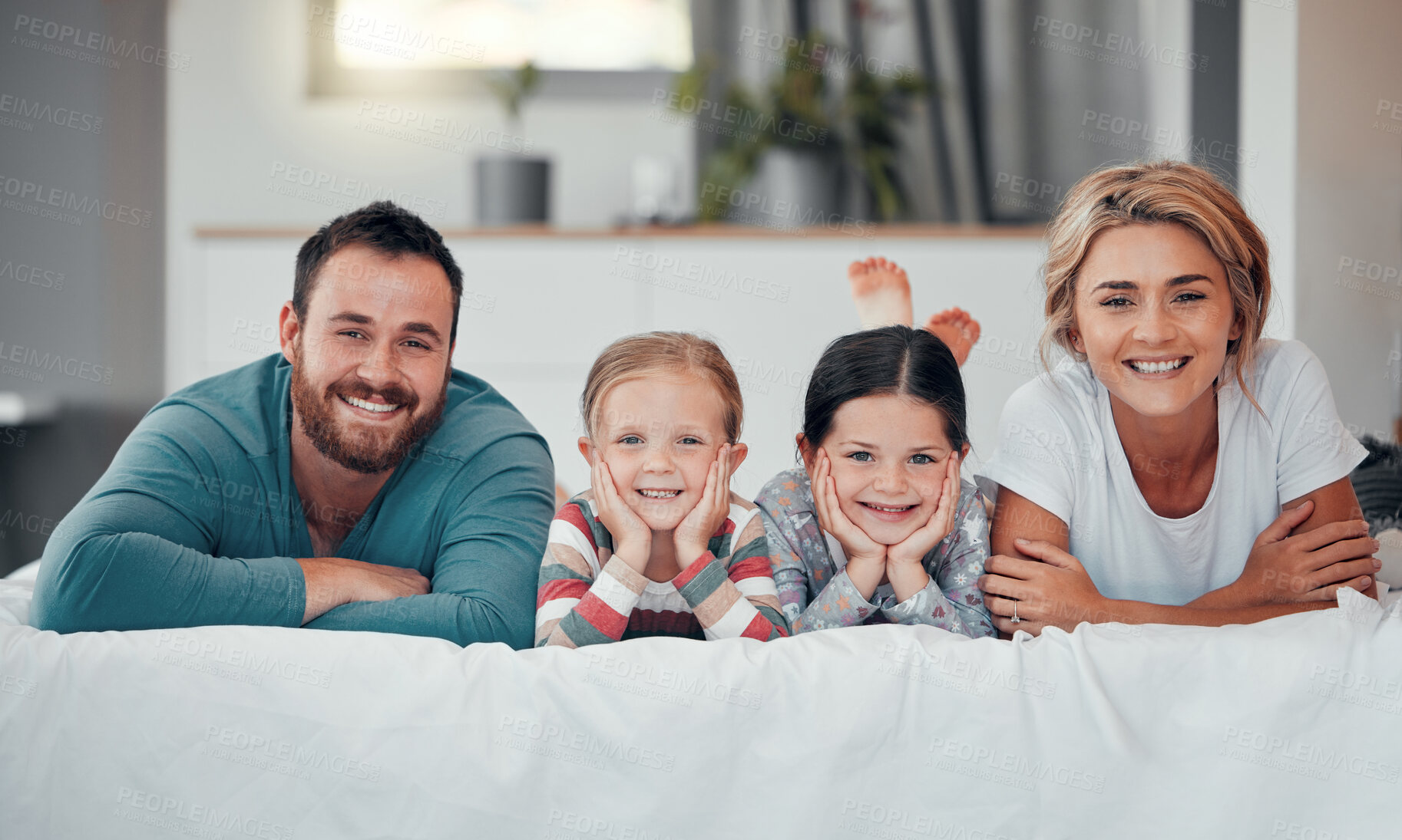 Buy stock photo Portrait of a smiling young caucasian family lying close together on the bed at home. Happy adorable girls bonding with their mother and father on a weekend. Happy couple and daughters in the morning