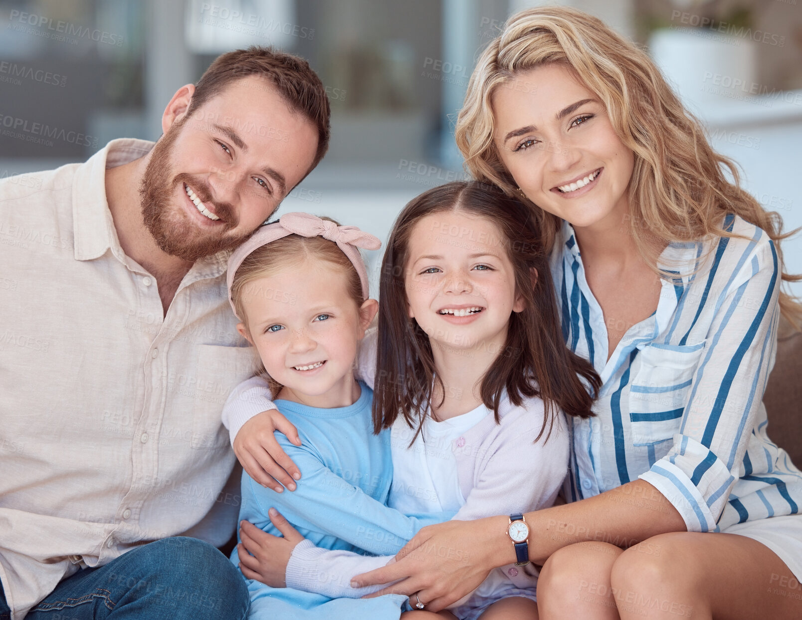 Buy stock photo Portrait of a smiling young caucasian family sitting close together on the sofa at home. Happy adorable girls hugging and bonding with their mother and father on a weekend. Happy couple and daughters