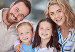 Portrait of happy young caucasian family sitting together in the living room smiling with healthy teeth at home. Adorable little girls hugging their mom and dad. Carefree parents and their two daughters at home