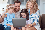 Happy young caucasian family sitting on a sofa at home and using a laptop to browse the internet. Adorable little girls bonding with mother and father while watching a movie. Family enjoying a show
