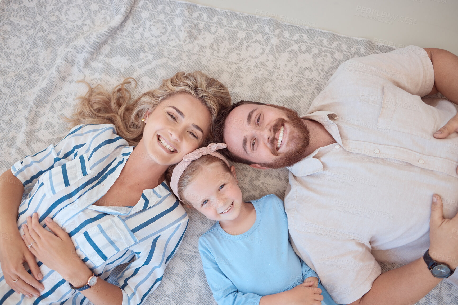 Buy stock photo Portrait of happy smiling caucasian family from above relaxing on a carpet floor at home. Carefree loving parents bonding with cute little daughter. Young girl spending quality time with mom and dad
