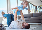 Happy little girl playing with her father in the lounge. Caucasian father lifting his daughter in the air, lying on the floor at home. Smiling parent having fun with his young daughter