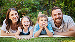 Portrait of cheerful caucasian family on a picnic lying on the lawn together. Happy couple with their two children spending time in nature. Little boy and girl having fun outside with parents
