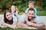 Portrait of happy caucasian family lying outside on grass and having a picnic. Cheerful parents and their two children lying on top of them having fun outdoors at park or backyard on a sunny day