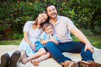 Portrait of a happy caucasian family having a picnic in their garden, sitting on a blanket. Cheerful parents relaxing, enjoying a summer day with their little son. Young family relaxing outside