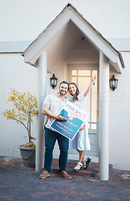 Young caucasian couple holding house keys while moving into new apartment. Happy man and woman holding for sale and sold sign outside home while relocating. Securing a loan for property or real estate