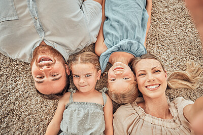 Above shot of a happy and loving family of four taking selfies while lying on their living room floor at home. A beautiful wife taking pictures with her husband, son and daughter while on a carpet