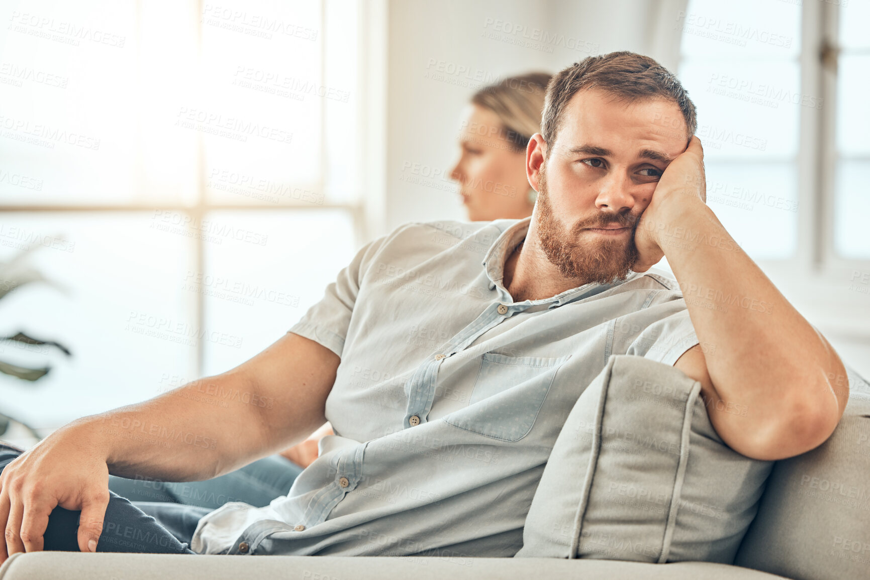 Buy stock photo Young caucasian man with a beard looking unhappy and annoyed while sitting on the couch during an argument with his wife at home. Bored man sitting and thinking on the couch. 
