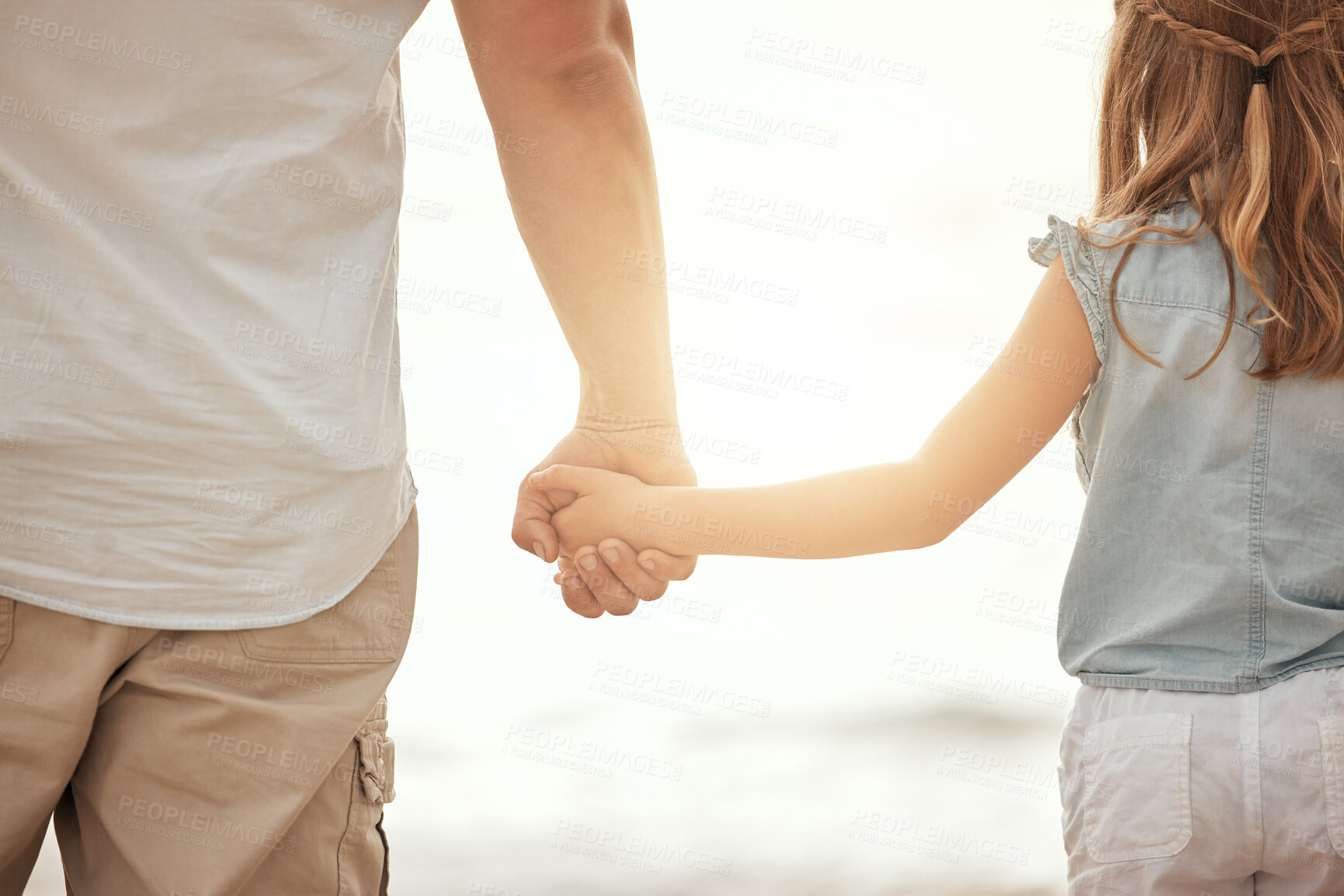 Buy stock photo Back of a father and daughter holding hands on the beach at sunset. Father bonding with his child, being affectionate and keeping her safe by holding her hand outside. Parent and child together 