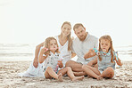 Happy caucasian family go four enjoying a vacation at at the beach. Young smiling couple playing in the sand with their two adorable daughters. Two cute sisters enjoying a summer day with mom and dad