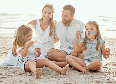 Cheerful caucasian family having fun together on beach. Cute cheerful little sisters blowing bubbles while relaxing and bonding and spending a day with their parents on the beach during the weekend