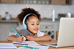 One mixed race preschool girl wearing headphones during video call with teacher on laptop for distance learning at home. Kid colouring with pencils during online virtual education class for homeschool