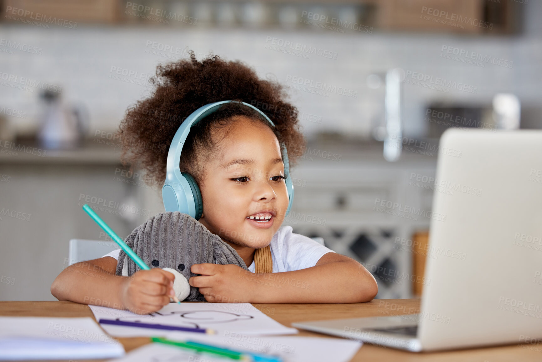 Buy stock photo One mixed race preschool girl wearing headphones during video call with teacher on laptop for distance learning at home. Kid colouring with pencils during online virtual education class for homeschool