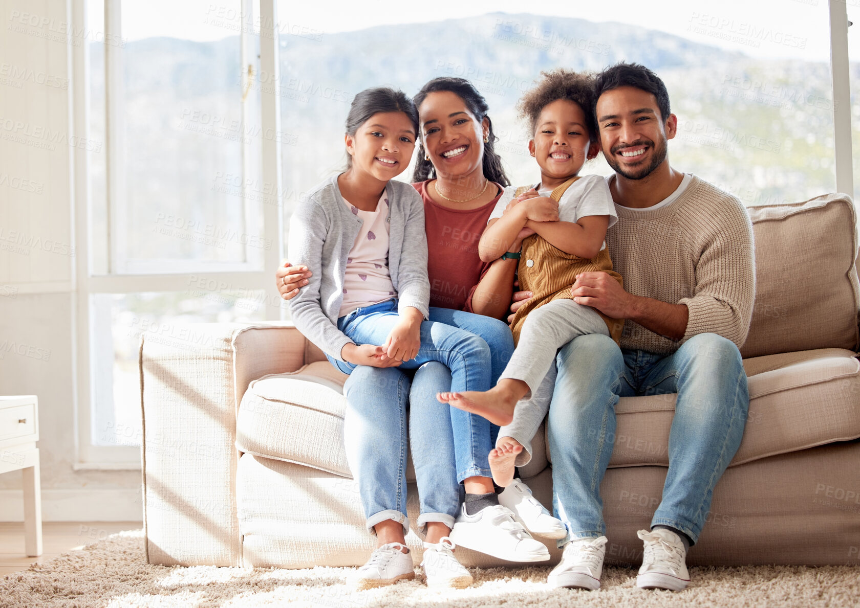 Buy stock photo Portrait of two happy parents bonding with their daughters in the lounge, sitting on the sofa. Smiling young family relaxing at home, enjoying time together. Mother and father holding their daughters