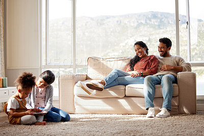 Buy stock photo Happy family relaxing at home. Smiling young parents with girls on a sofa, watching their cute little children play and have fun with a digital tablet on the floor in the living room with a window