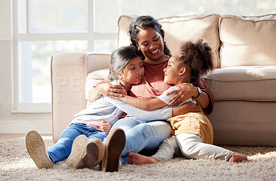 Mixed race mother hugging her daughters in the living room at home. Indian woman showing love and affection to her girls. Hispanic siblings embracing their single parent during free time on a weekend