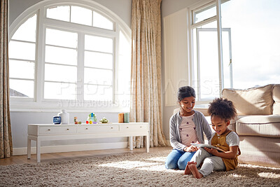 Buy stock photo Two sisters playing games in the living room. Adorable mixed race girl siblings using a tablet while sitting on the floor at home. Happy young children surfing the net while in the lounge. 