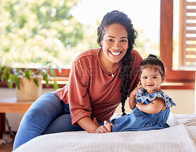 Buy stock photo Portrait of young mixed race mother sitting with her adorable baby girl on the bed in a bedroom at home. Hispanic woman spending time with her cute little daughter on a bed at home