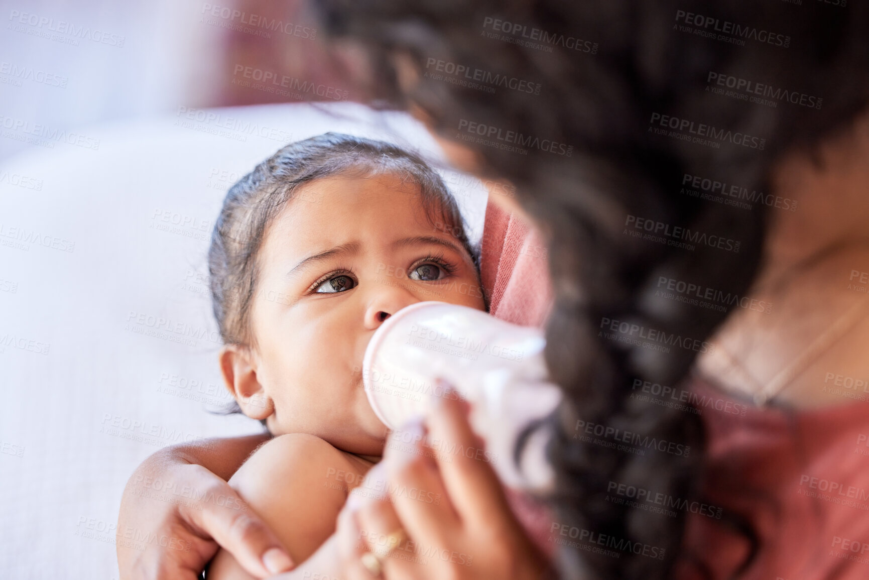 Buy stock photo Hispanic mother feeding her little baby girl a bottle of milk formula. Tiny baby and mother bonding in the nursery together while drinking a bottle of milk. Mother holding her baby in the bedroom