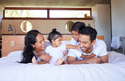 Happy young family of four smiling and having fun in bed together at home. Young mixed race couple bonding with their two daughters and laughing together while looking comfortable in bed
