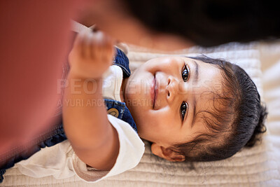 Above face of an adorable baby girl smiling at her mother. Infant daughter lying on the bed and looking up lovingly at her mom at home. Mixed race chid and her parent bonding in the bedroom