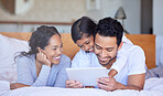 A young mixed race family smiling and relaxing on the bed at home using a digital tablet.Two hispanic parents and their cute daughter watching videos on a wireless device while lying on the bed at home