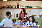 Happy mixed race mother cooking in the kitchen for her family. Dad working from home with laptop while kids do homework or being homeschooled. Family of five at home during coronavirus pandemic 