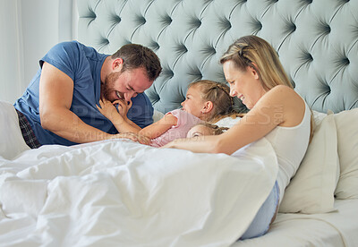 Happy caucasian family lying in bed with two daughters. Two little girls looking happy while being playful and affectionate with their young smiling parents. Family of four in a big comfortable bed