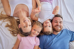 Above happy parents with little children lying on a bed at home and looking up. Caucasian girls bonding with their mother and father. Smiling young married couple enjoying free time with daughters