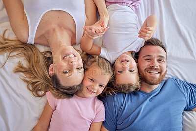 Buy stock photo Above happy parents with little children lying on a bed at home and looking up. Caucasian girls bonding with their mother and father. Smiling young married couple enjoying free time with daughters