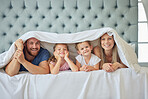 Portrait of happy parents with little children lying on bed at home under blanket. Caucasian girls bonding with their mother and father. Smiling young married couple enjoying free time with daughters