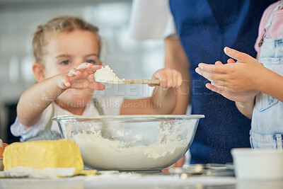 Buy stock photo Little girl holding a spoon of flour. Family baking together at home. Two sisters baking with a parent. Caucasian girl putting flour into a bowl. Mother baking with her daughters. Siblings baking . 