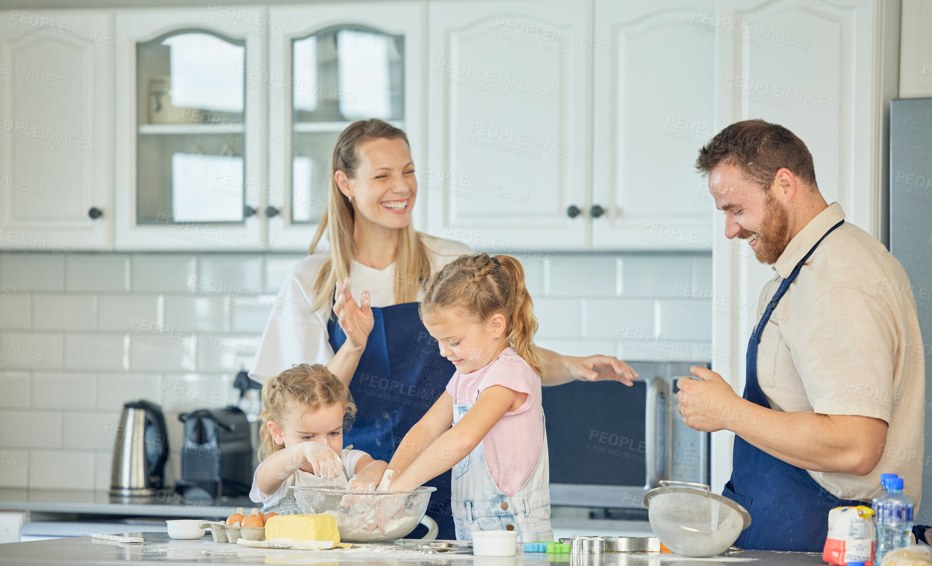 Buy stock photo Happy caucasian parents and their little daughters baking together in a kitchen at home. Mother and father teaching their girls how to make dough in a messy kitchen. Sisters learning how to bake