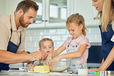 Caucasian caring parents and their little daughters baking together in a kitchen at home. Mother and father teaching their girls how to make dough in a messy kitchen. Sisters learning how to bake