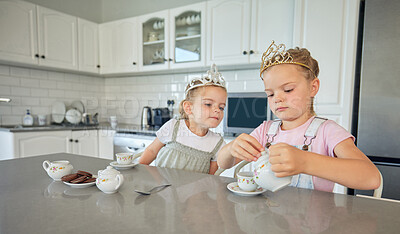 Two little girls having a tea party at home. Sibling sister friends wearing tiaras while playing with tea set and having cookies at kitchen table. Sisters getting along and playing together