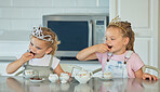 Two little girls having a princess tea party at home. Sibling sister friends wearing tiaras while playing with tea set and having cookies at kitchen table. Sisters getting along and playing together 