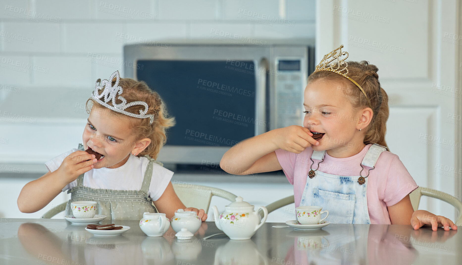 Buy stock photo Two little girls having a princess tea party at home. Sibling sister friends wearing tiaras while playing with tea set and having cookies at kitchen table. Sisters getting along and playing together