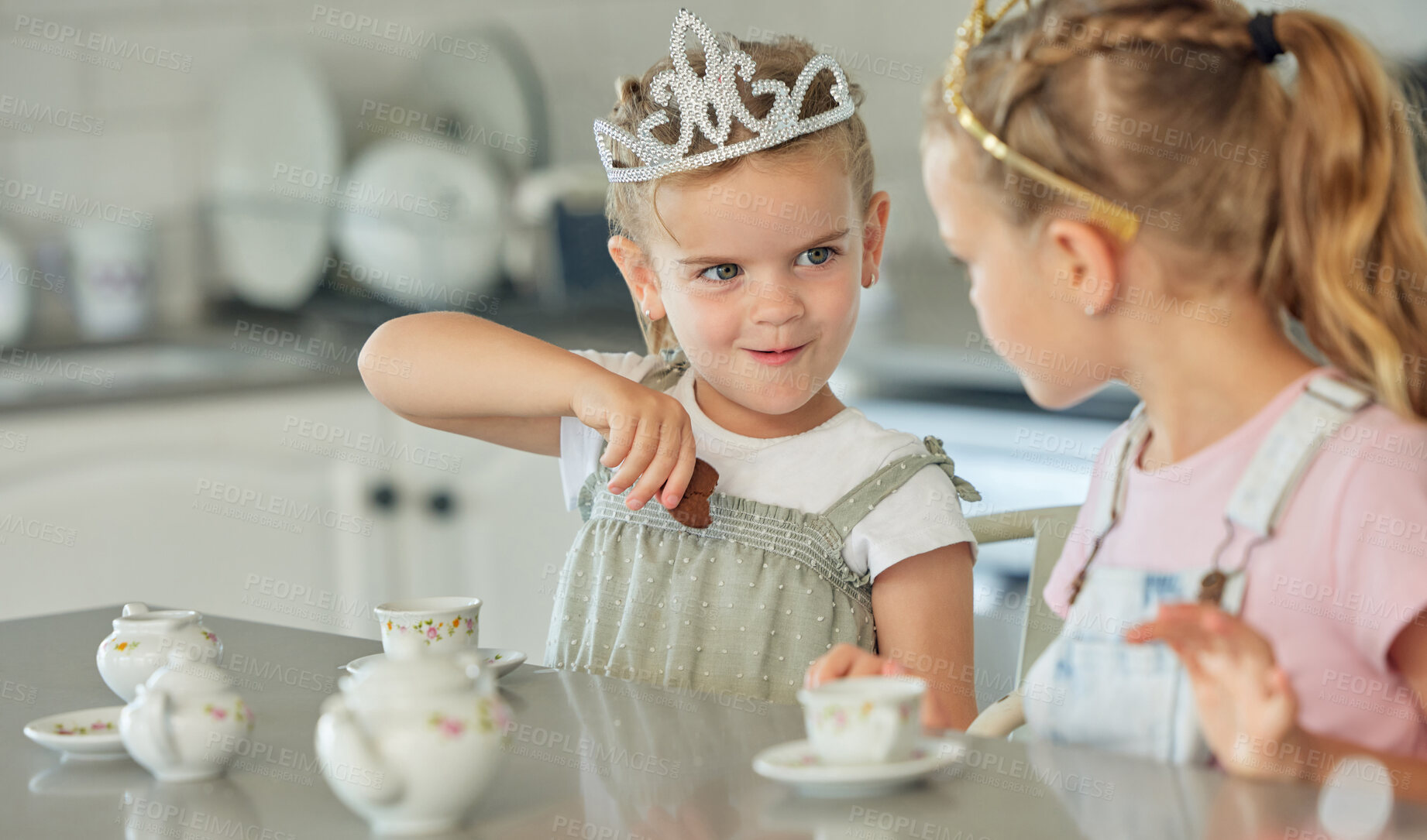 Buy stock photo Two little girls having a princess tea party at home. Sibling sister friends wearing tiaras while playing with tea set and having cookies at kitchen table. Sisters getting along and playing together 