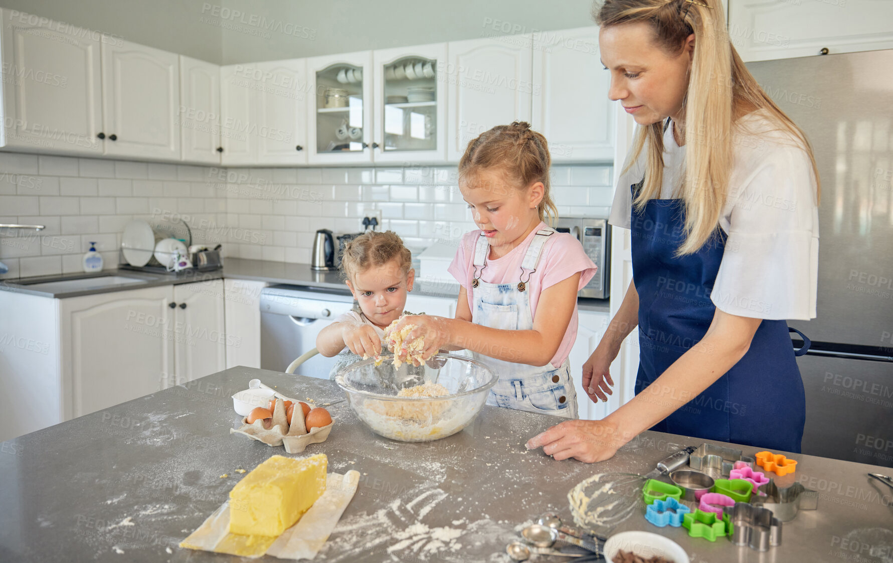 Buy stock photo Caucasian mother and little daughters baking together in a kitchen at home. Mom teaching girls how to make dough in a messy kitchen. Sisters learning how to bake with their mom