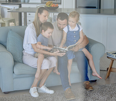 Caucasian family reading a book together on the couch at home. Mother and father teaching their little son and daughter how to read. Brother and sister learning to read with their parents
