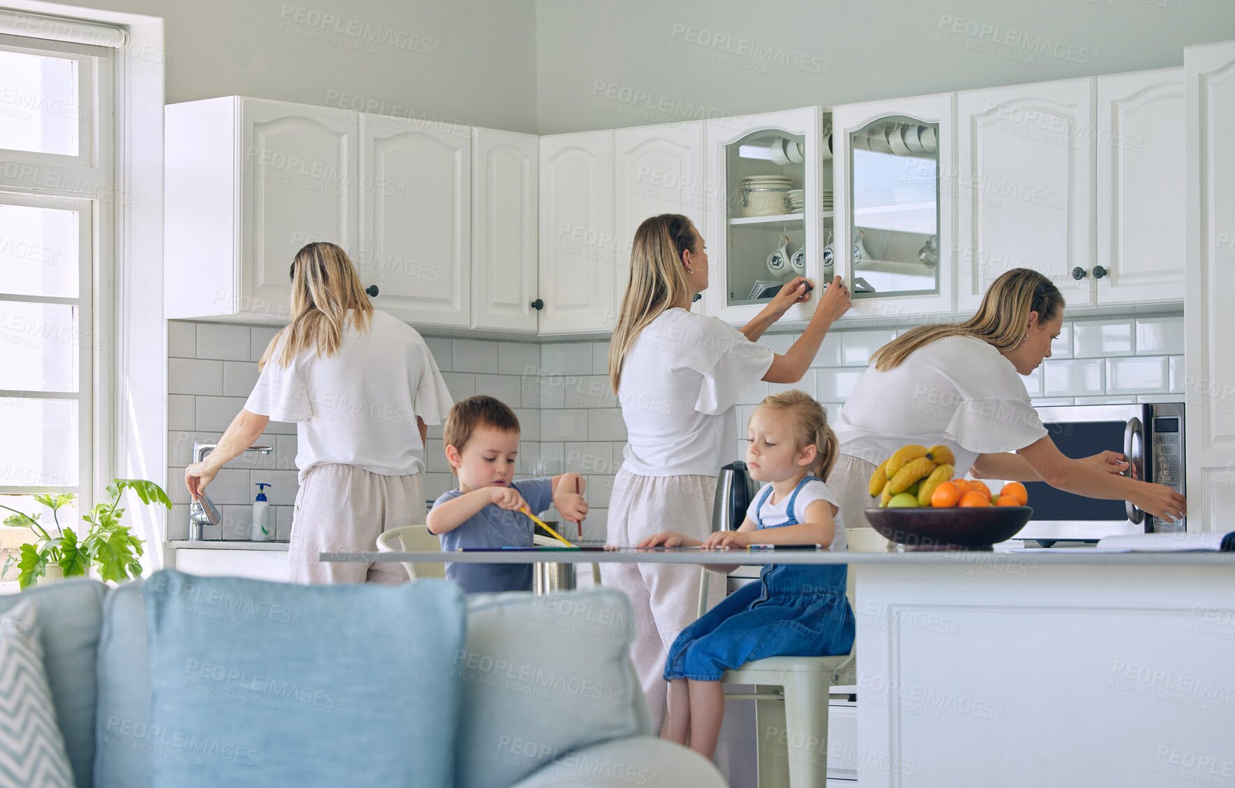 Buy stock photo Busy mom feeding kids and cleaning the house. Little girl and boy sitting and eating in the kitchen while mother does chores. Stay-at-home mother multitasking and being a super mom