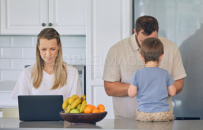 Happy young caucasian family having lunch time with fresh fruit in a bright kitchen. Beautiful young mother and father feeding their cute son fruit while using a laptop at home